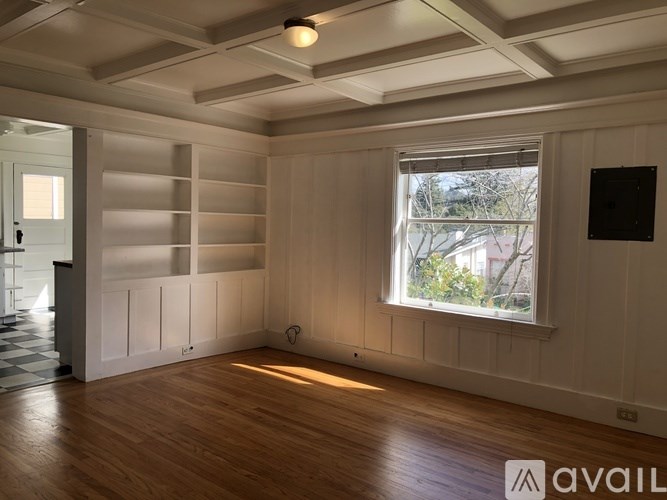 A room with wooden floors and a window showing a view of trees and a building outside.