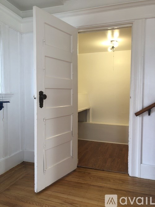 A white door with a black handle is open to a hallway.