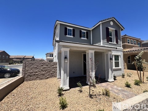A modern house with a grey and white exterior and a stone wall in the front yard.