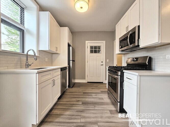 A kitchen with white cabinets and appliances, a sink, and a door in the background.