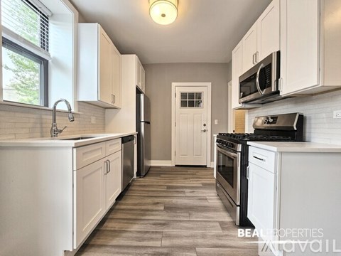 A kitchen with white cabinets and appliances, a sink, and a door in the background.