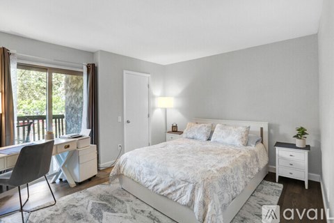 A bedroom with a large bed, a desk with a chair, and a window with curtains.