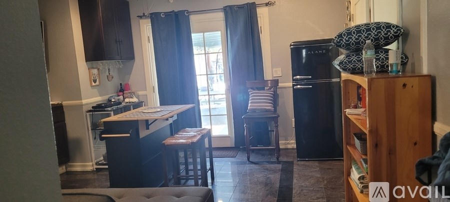 A kitchen with a black fridge and a window with curtains.