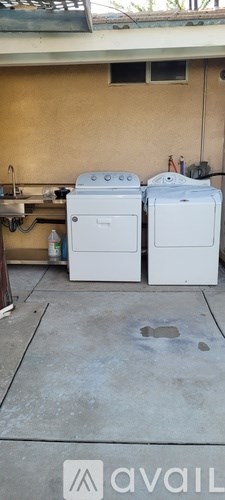 Two white washing machines are outside a yellow building.