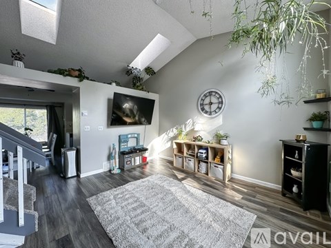 A living room with a grey rug and a clock on the wall.