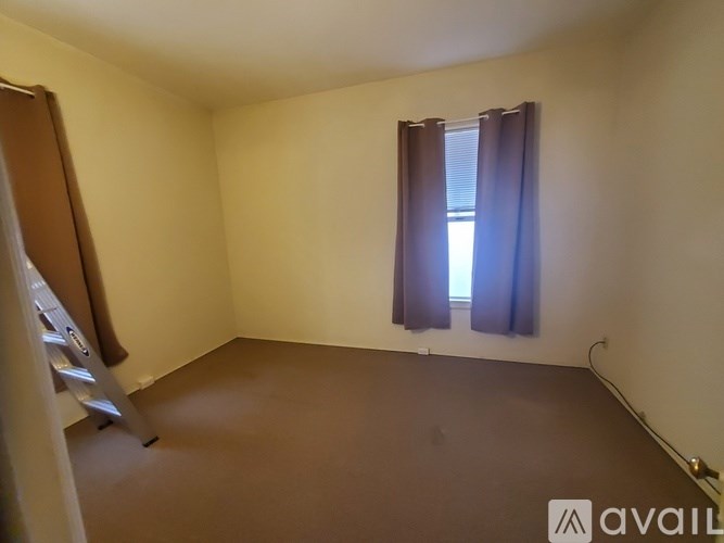 A room with a brown carpet and a window with brown curtains.
