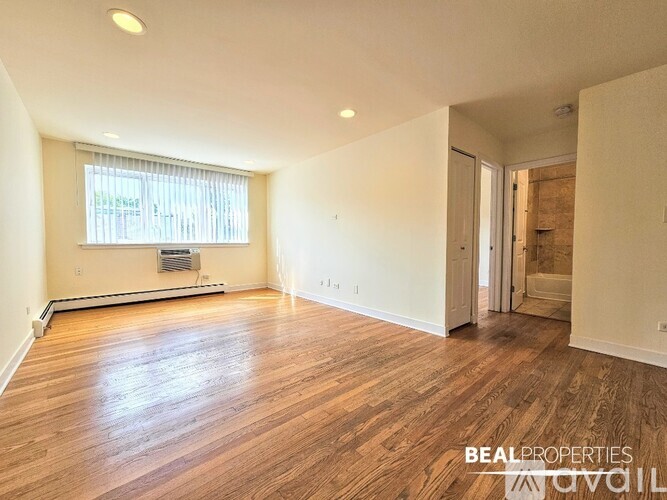 A spacious room with wooden floors and a window with blinds.