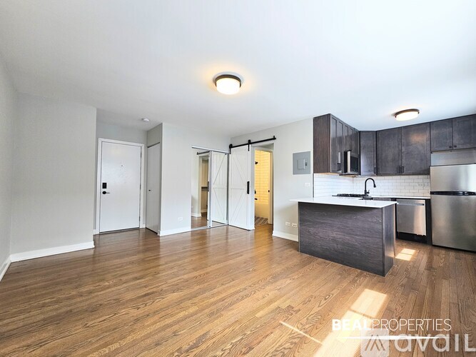 A spacious room with wooden flooring and a window with an air conditioning unit beneath it.