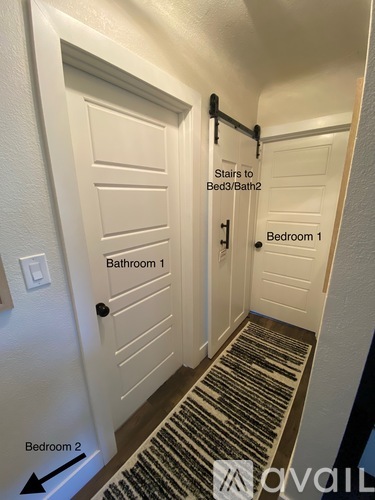 A hallway with a black and white striped carpet and a sign that says "Stairs to Bed3/Bath2" and "Bedroom 1" and "Bathroom 1" and "Bedroom 