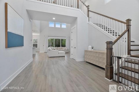 A spacious living room with a staircase and a painting on the wall.