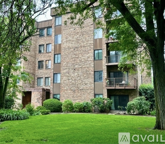 A tall building with a balcony on the second floor is surrounded by greenery.