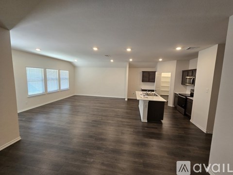 A spacious room with wooden flooring and a kitchen area in the background.