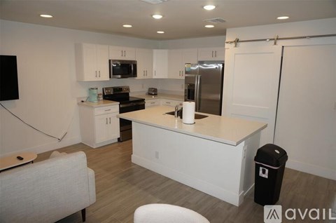 A kitchen with white cabinets and a white island with a black trash can.