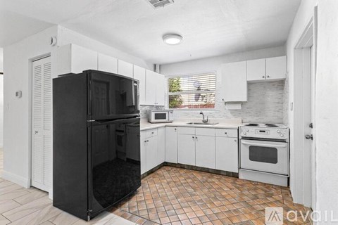 A black refrigerator is in a kitchen with white cabinets and a tiled floor.