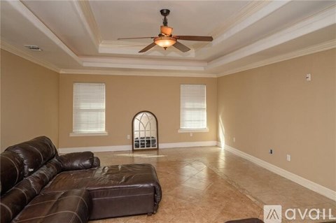 A living room with a brown leather couch and a ceiling fan.