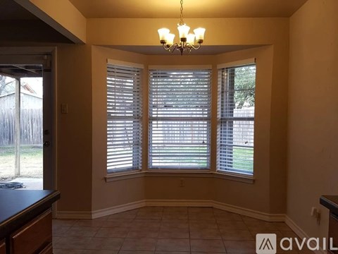 A room with a chandelier, a window with blinds, and a fence outside.