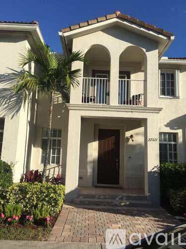 A white two-story house with a balcony and a brown door.