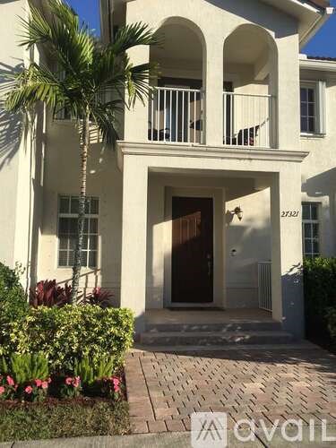 A white two-story house with a balcony and a brown door.