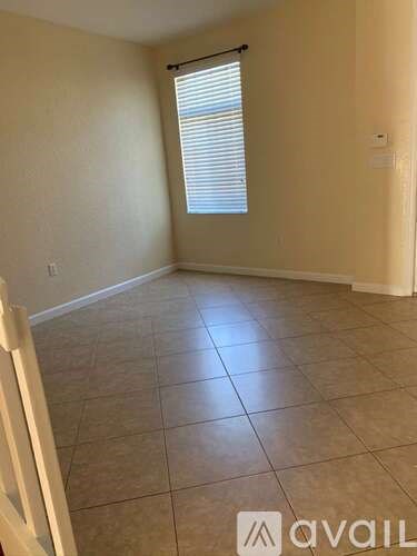 A room with beige walls and tiled flooring with a window covered by blinds.