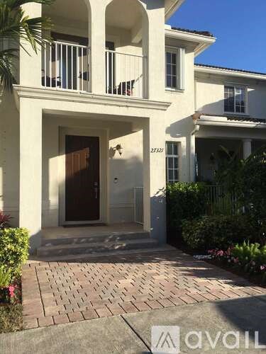 A white two-story house with a balcony and a brown door.