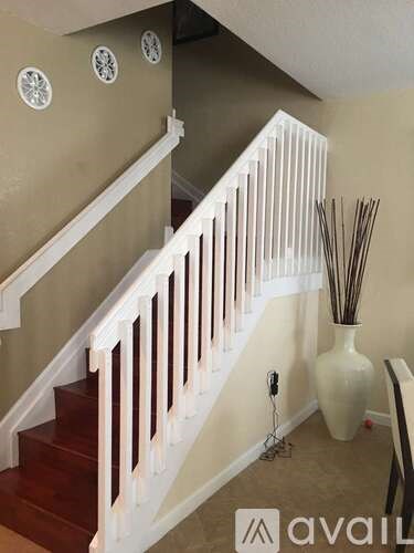 A staircase with a white railing and a vase on the floor.