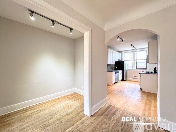 A spacious room with wooden flooring and a kitchen area in the background.