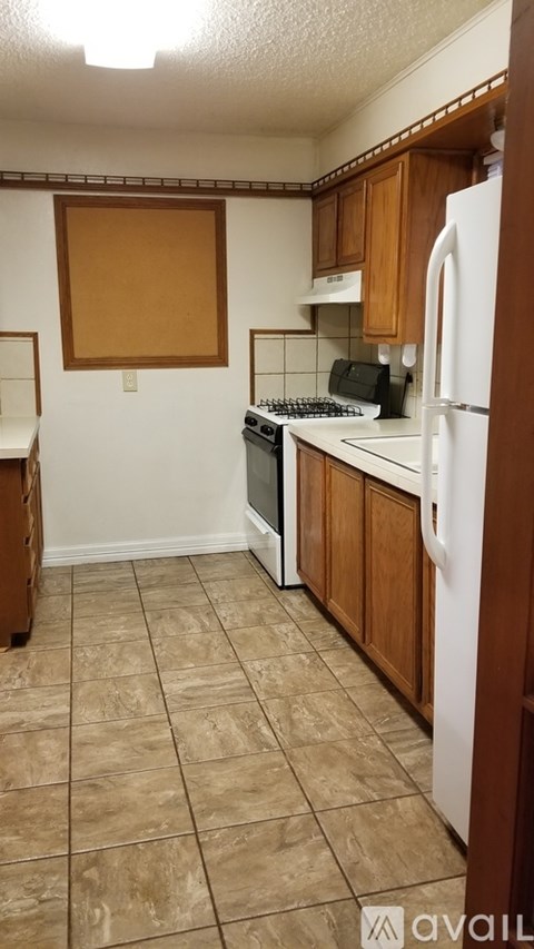 A kitchen with a white refrigerator, wooden cabinets, and a tiled floor.