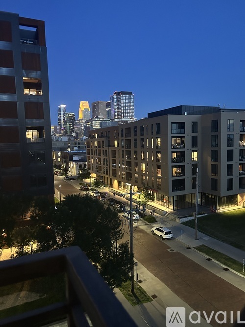 A cityscape at dusk with apartment buildings and a car on the street.