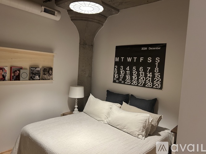 A bedroom with a bed, lamp, and a calendar on the wall.
