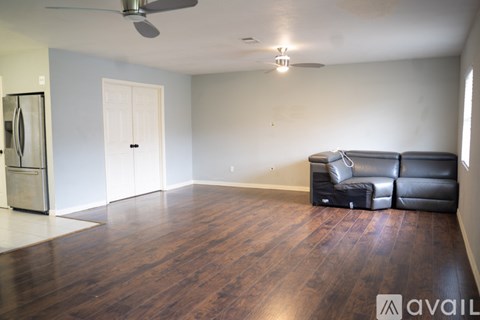 A living room with a black leather couch and a ceiling fan.