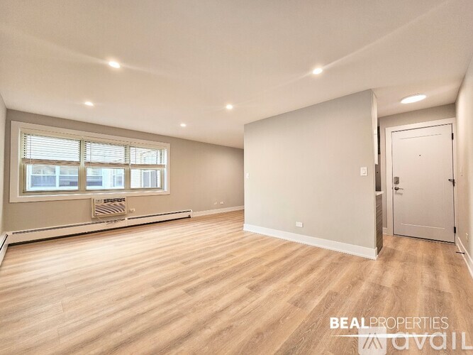 A spacious room with wooden flooring and a window with blinds.