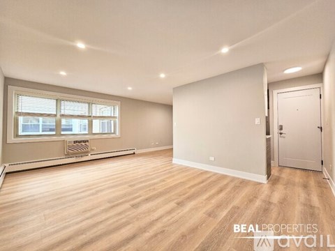 A spacious room with wooden flooring and a window with blinds.