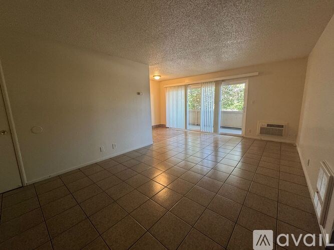 A spacious room with tiled flooring and a sliding glass door leading to a balcony.