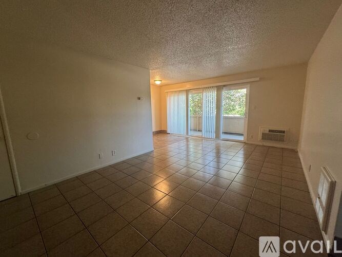 A spacious room with tiled flooring and a sliding glass door leading to a balcony.