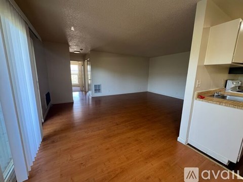 A room with wooden floors and white walls, with a kitchen area to the right.