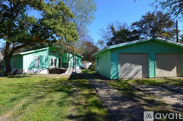 A green building with a white door and windows is surrounded by a grassy area.