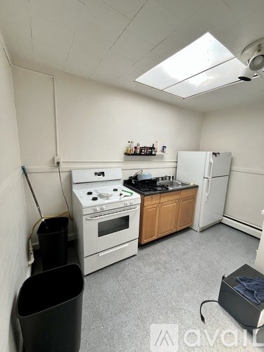 A small kitchen with a black trash can and a black box on the floor.