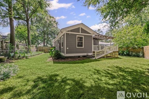 A small house with a porch is surrounded by a green lawn and trees.