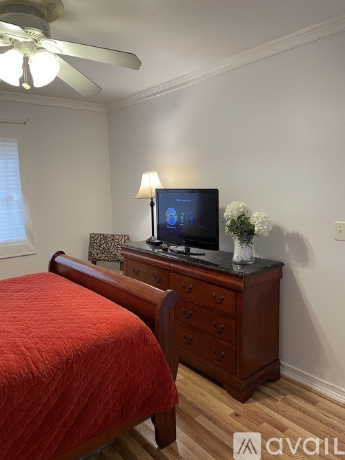 A bedroom with a red bedspread and a television on a wooden dresser.