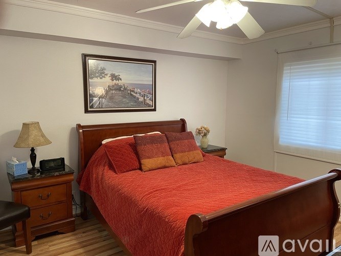 A bedroom with a red bedspread and a painting on the wall.