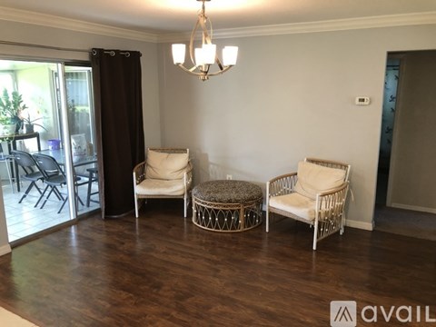 A living room with a white chair and ottoman, a brown wicker chair, and a chandelier.