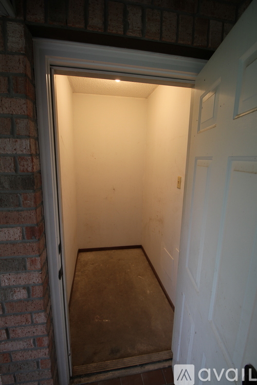 A white door is open to a small, empty room with brick walls.