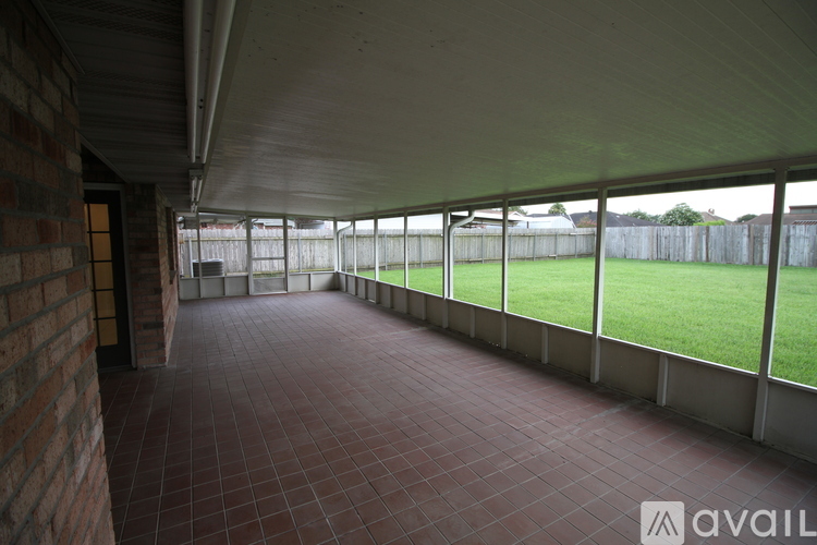 A long covered walkway with brick flooring and a view of a green yard outside.
