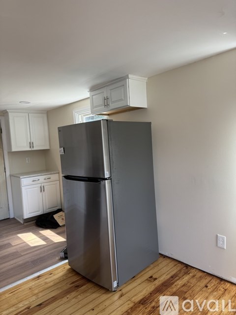 A silver refrigerator in a kitchen with wooden floors and white cabinets.