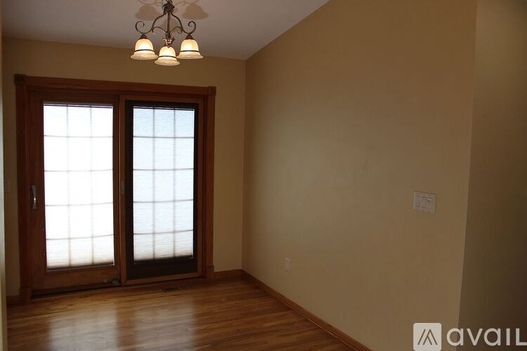A room with a wooden floor, a ceiling fan with lights, and a window with a glass door.