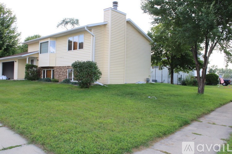 A house with a beige siding and a brown door is surrounded by a green lawn.