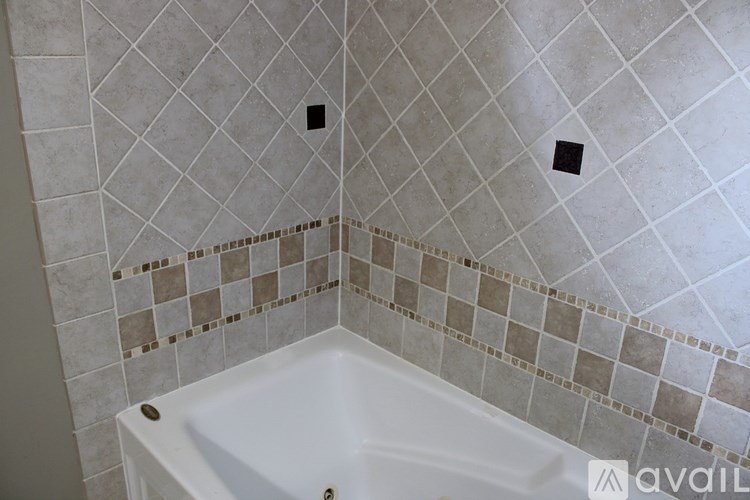 A white bathtub with brown and beige tiles on the wall.