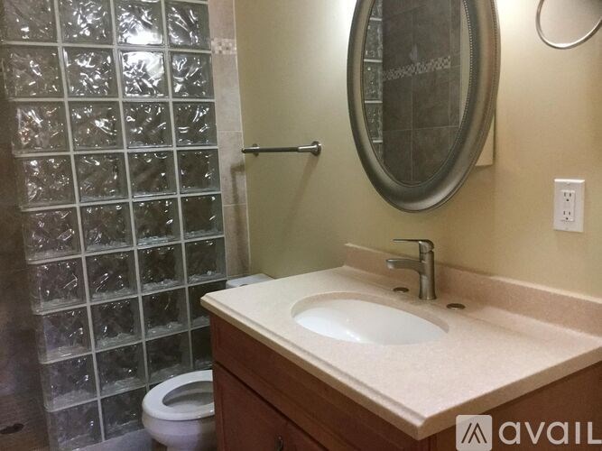 A bathroom with a sink, mirror, and shower with a glass block wall.