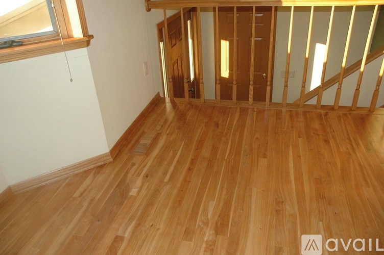 A room with wooden flooring and a staircase in the background.