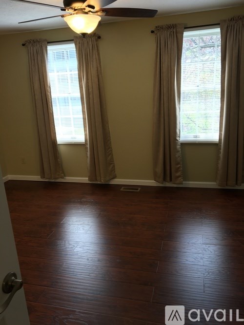 A room with a ceiling fan and two windows with curtains.